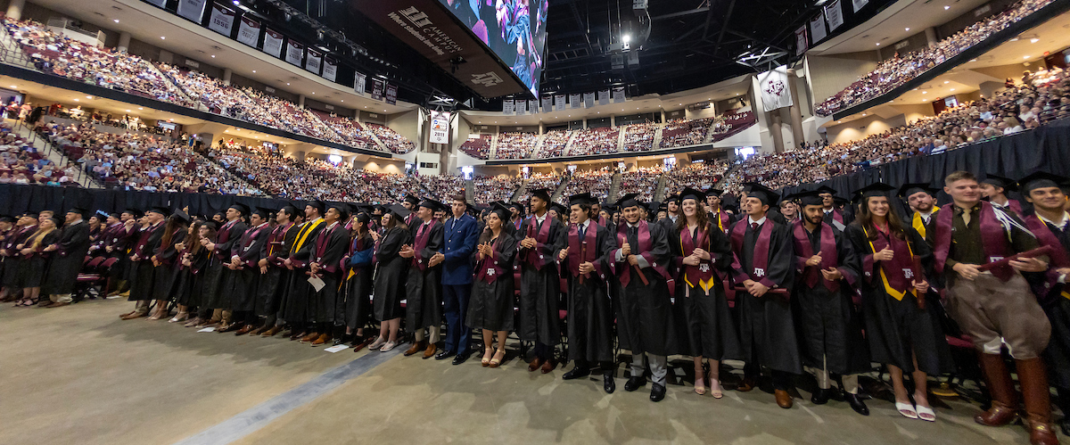 Aggies standing with their diplomas at graduation, becoming former students